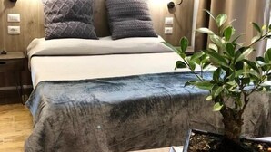 A bedroom with a bed, two wall-mounted lamps, a potted plant, and a nightstand. - Arya Cagliari (Cagliari)