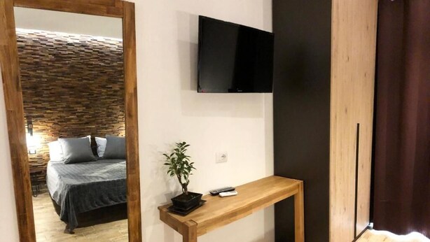 A room with a bed, a TV mounted on the wall, a wooden console table, and a potted plant. - Arya Cagliari (Cagliari)