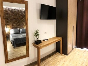 Une pièce comprenant un lit, un téléviseur fixé au mur, une console en bois et une plante en pot.