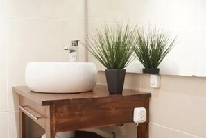 Une salle de bain avec un lavabo blanc, un meuble-lavabo en bois et deux plantes en pot.