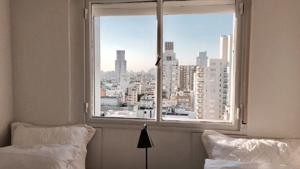 Une chambre d’hôtel avec un lit, une table de chevet avec une lampe et une fenêtre donnant sur la ville.