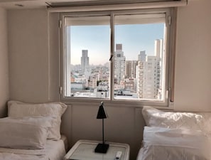 Une chambre d’hôtel avec un lit, une table de chevet avec une lampe et une fenêtre donnant sur la ville.