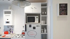 Une cuisine de taille réduite, avec des meubles blancs, un four à micro-ondes, un réfrigérateur et une cuisinière à gaz.