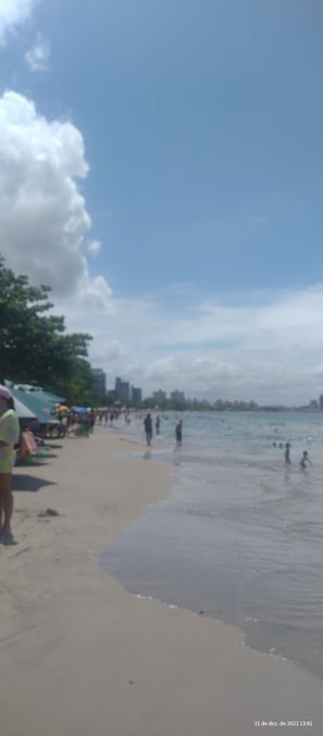 Une plage où l’on voit des gens se promener et jouer dans l’eau, un rivage sablonneux et quelques tentes en arrière-plan.