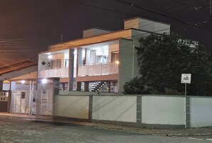 Um edifício moderno de dois andares com portão fechado, varanda no andar superior e placa indicando área de estacionamento.