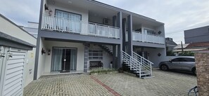 A two-story residential building with a covered outdoor area, a staircase, and a car parked in front. - Apart ZSS (Penha)