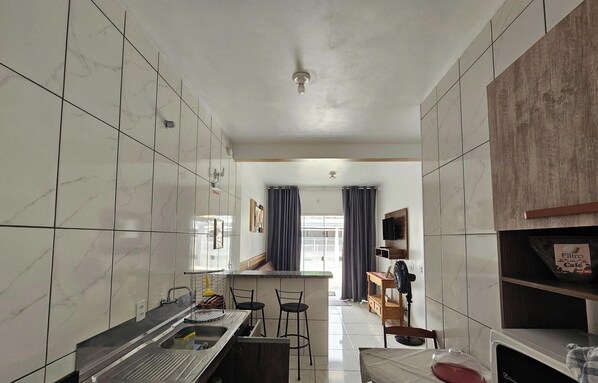 Cocina compacta con isla central, taburetes de bar y zona de comedor con televisor.