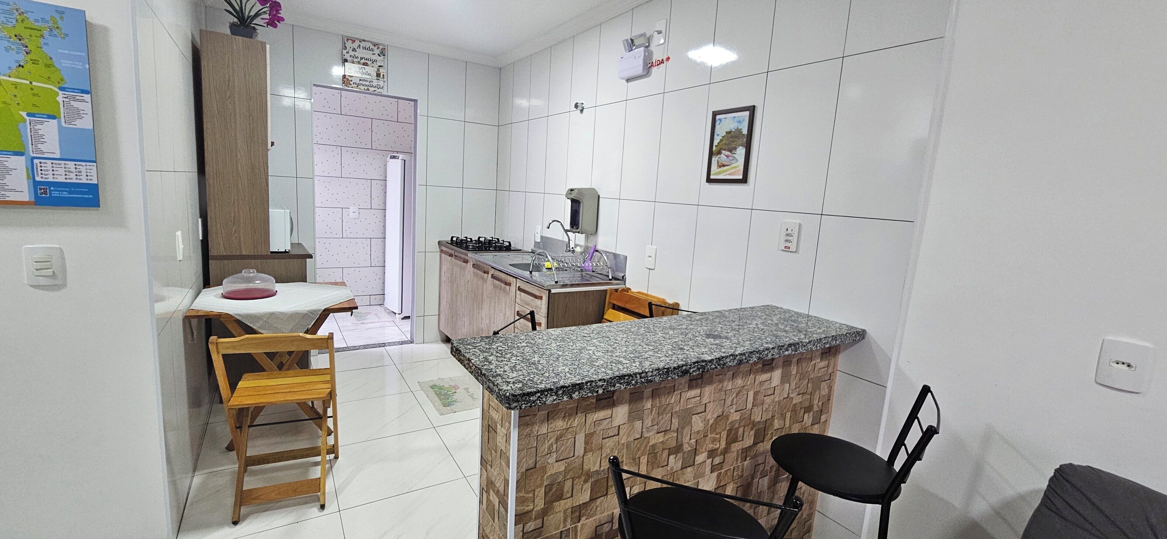Cocina compacta con encimera de granito, armarios de madera y una zona de comedor con mesa y sillas.