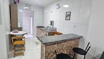 Cocina compacta con encimera de granito, armarios de madera y una zona de comedor con mesa y sillas.