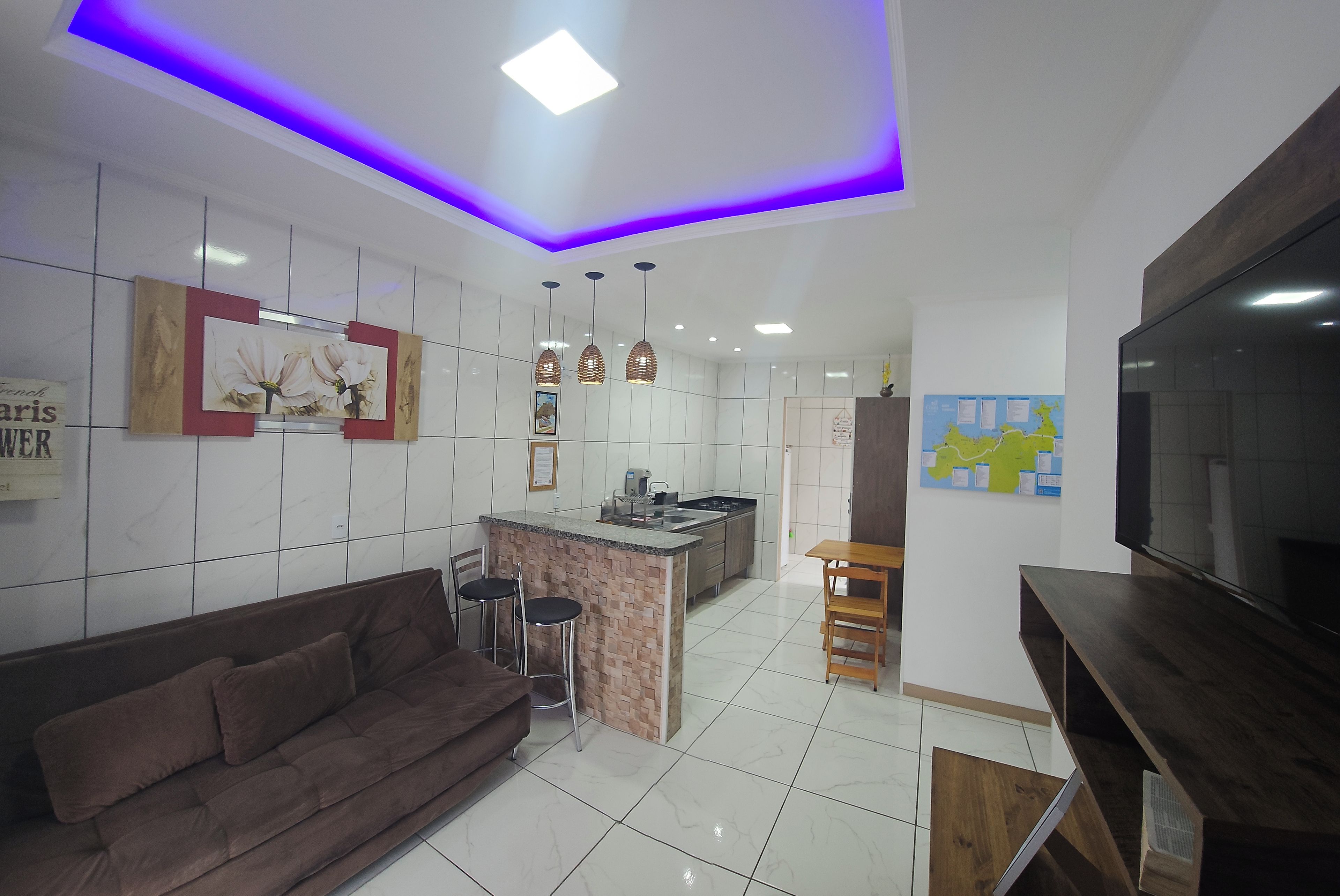 A modern kitchen with a central island, a dining area with a brown sofa and chairs, and a flat-screen TV mounted on the wall.