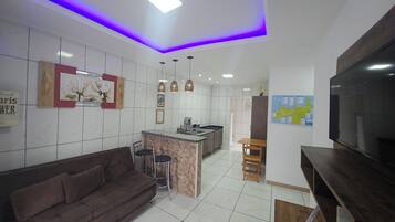 A modern kitchen with a central island, a dining area with a brown sofa and chairs, and a flat-screen TV mounted on the wall.