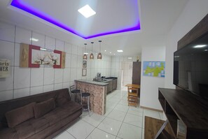 A modern kitchen with a central island, a dining area with a brown sofa and chairs, and a flat-screen TV mounted on the wall. - Apart ZSS (Penha)