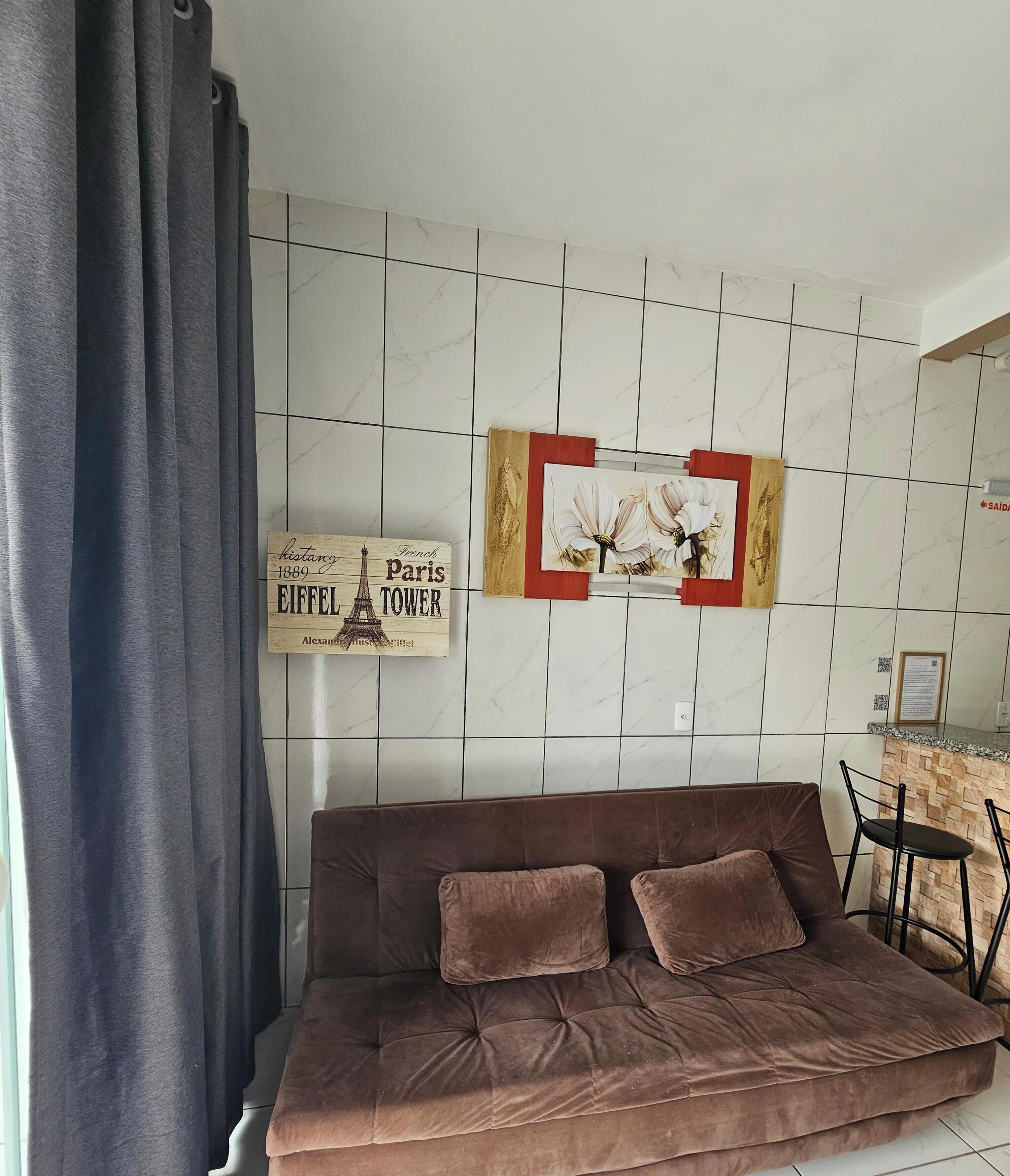 Una sala de estar con un sofá marrón, un letrero de la Torre Eiffel colgado en la pared y un cuadro con flores.