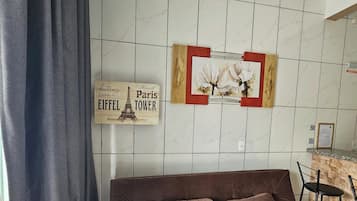Una sala de estar con un sofá marrón, un letrero de la Torre Eiffel colgado en la pared y un cuadro con flores.