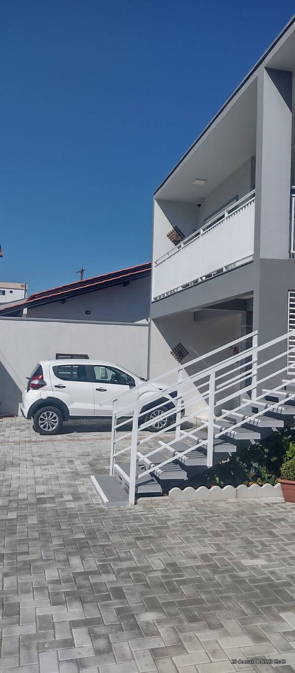 A modern building with a white exterior, a staircase leading to a balcony, and a parked white car.