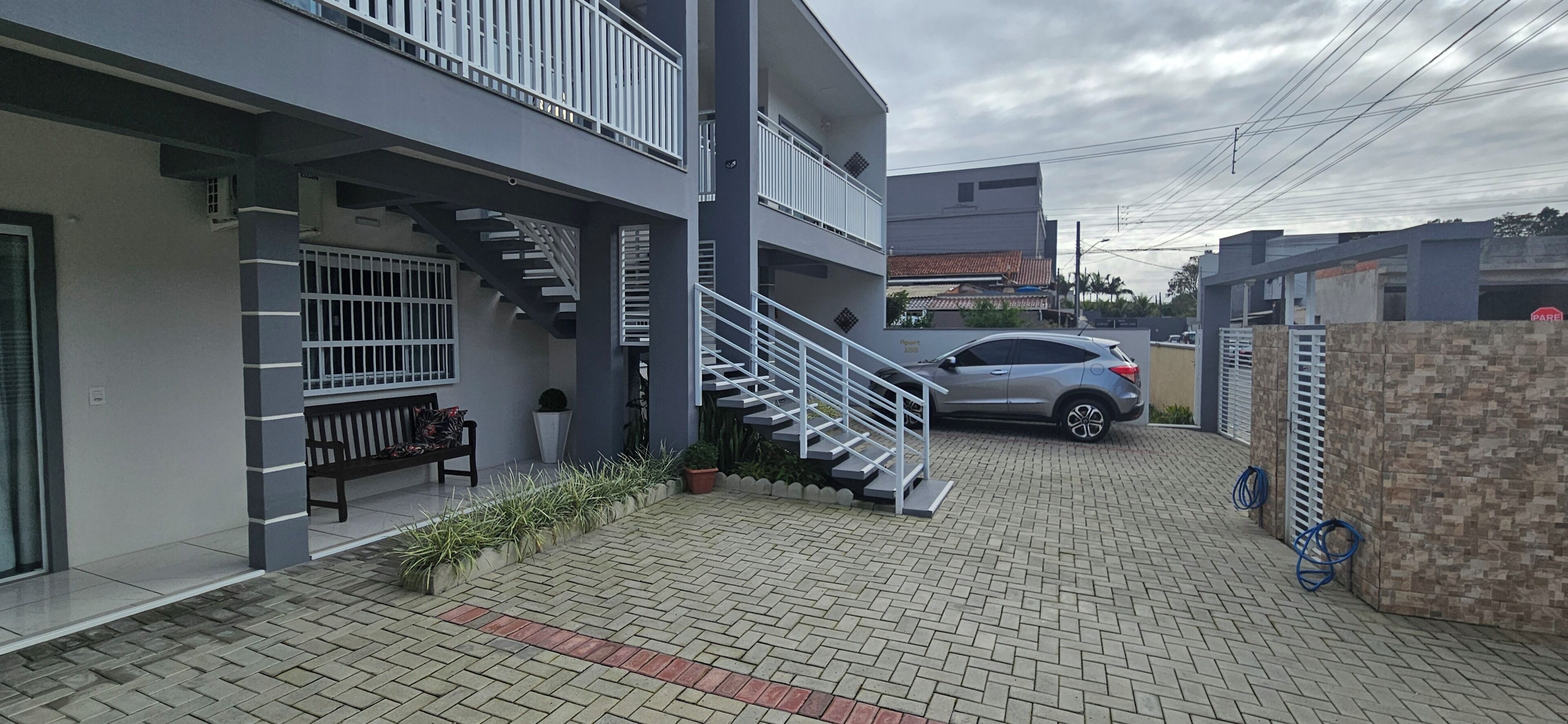 Um edifício moderno com uma escadaria, um carro estacionado em frente e um caminho de acesso pavimentado.