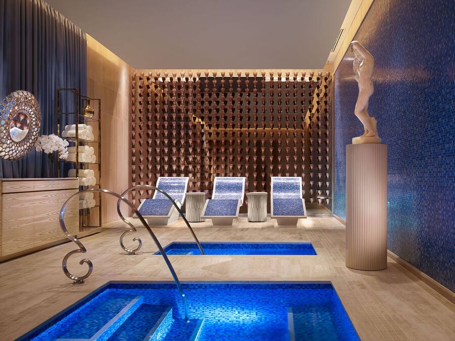 Een moderne spa met een zwembad, ligbedden en een wand met hangende vazen.