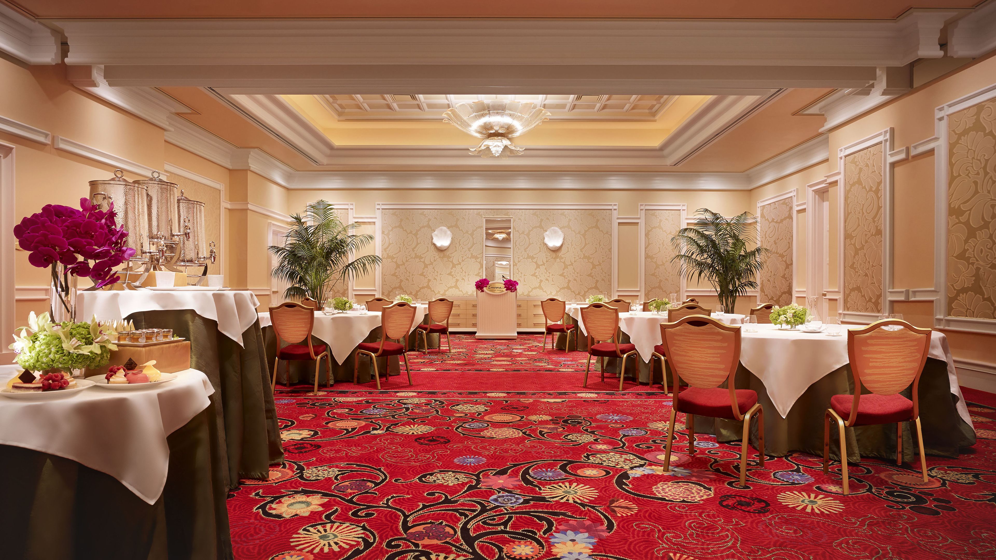 Une salle à manger élégante, dotée de plusieurs tables, d’un tapis rouge et de décorations ornementales au plafond.