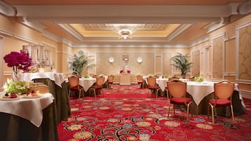 Une salle à manger élégante, dotée de plusieurs tables, d’un tapis rouge et de décorations ornementales au plafond.