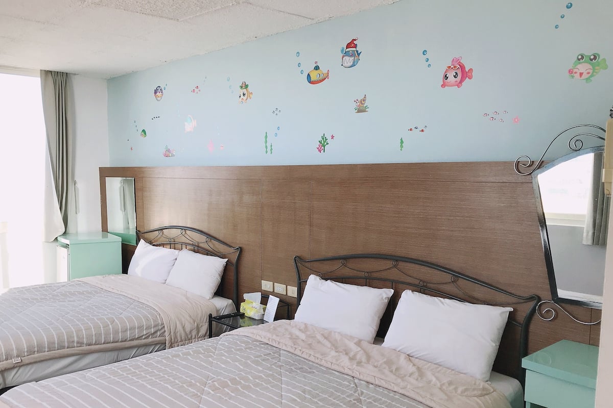 Habitación de hotel con dos camas, cabecero de madera, espejo y una pared decorada con motivos marinos.