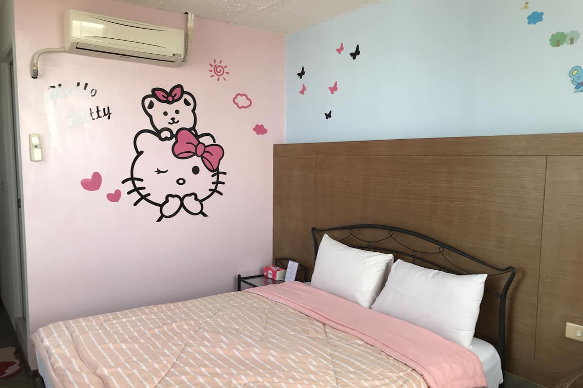 Un dormitorio con pared rosa, un adhesivo de Hello Kitty, una cama con colcha a rayas rosada y blanca, y un cabecero de madera.