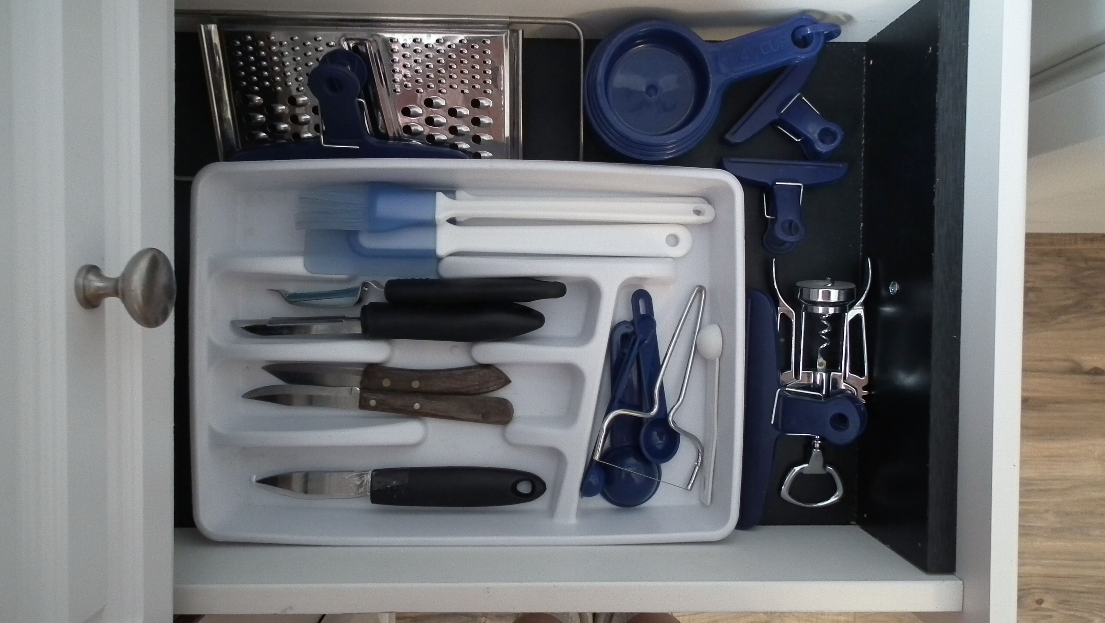 A drawer containing various kitchen utensils and tools, including knives, a grater, and a measuring cup.