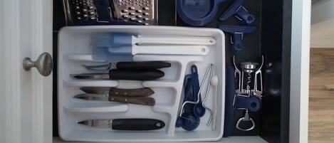 A drawer containing various kitchen utensils and tools, including knives, a grater, and a measuring cup.