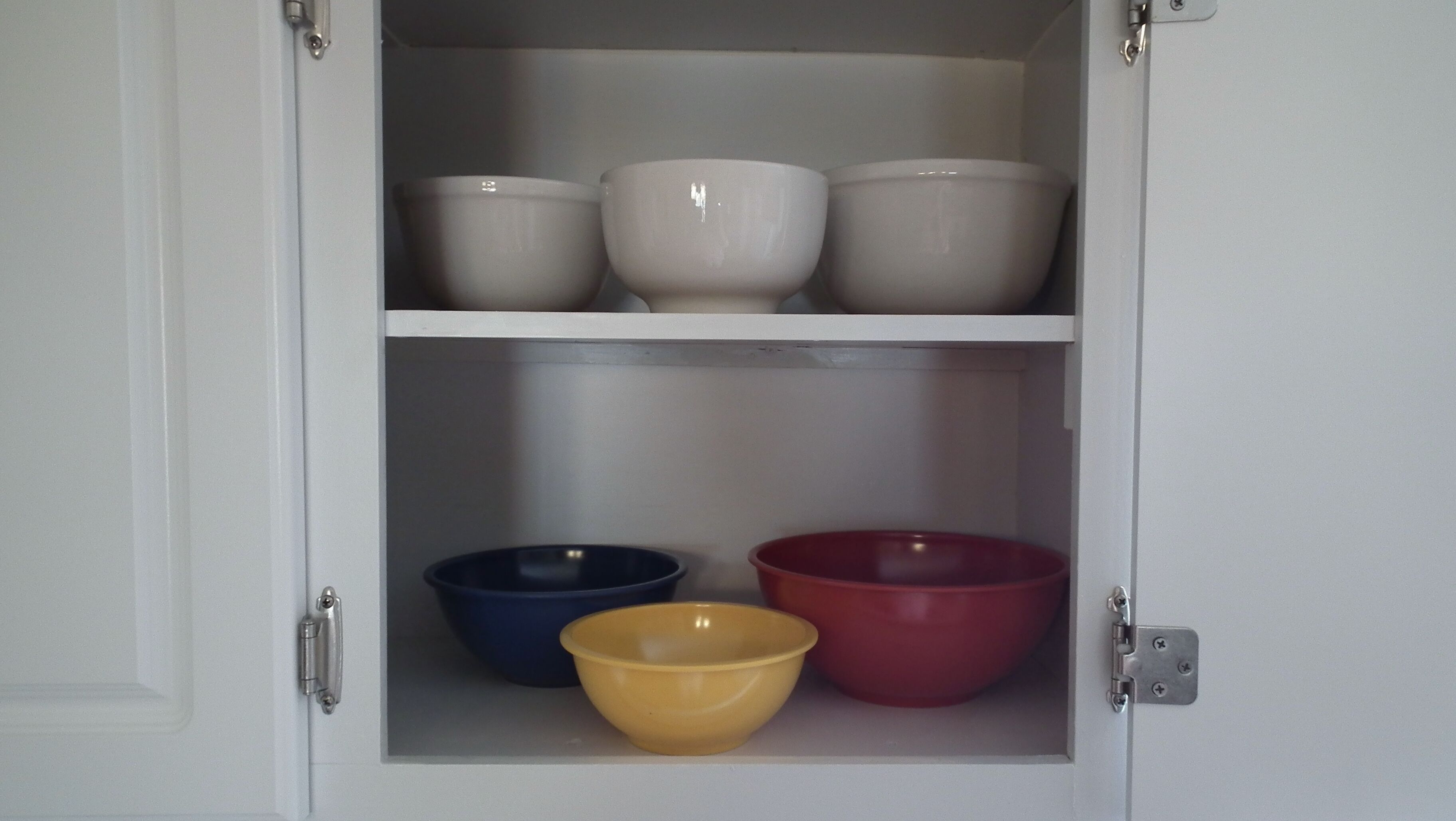 A cabinet with three shelves, each holding bowls of different colors.