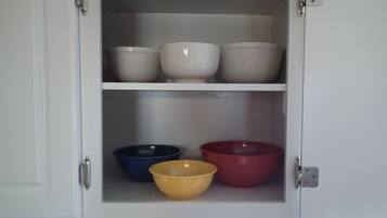 A cabinet with three shelves, each holding bowls of different colors.
