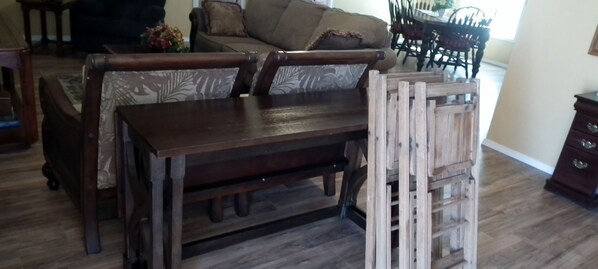 A wooden dining table with chairs, a sofa, and a wooden ladder in a living room.