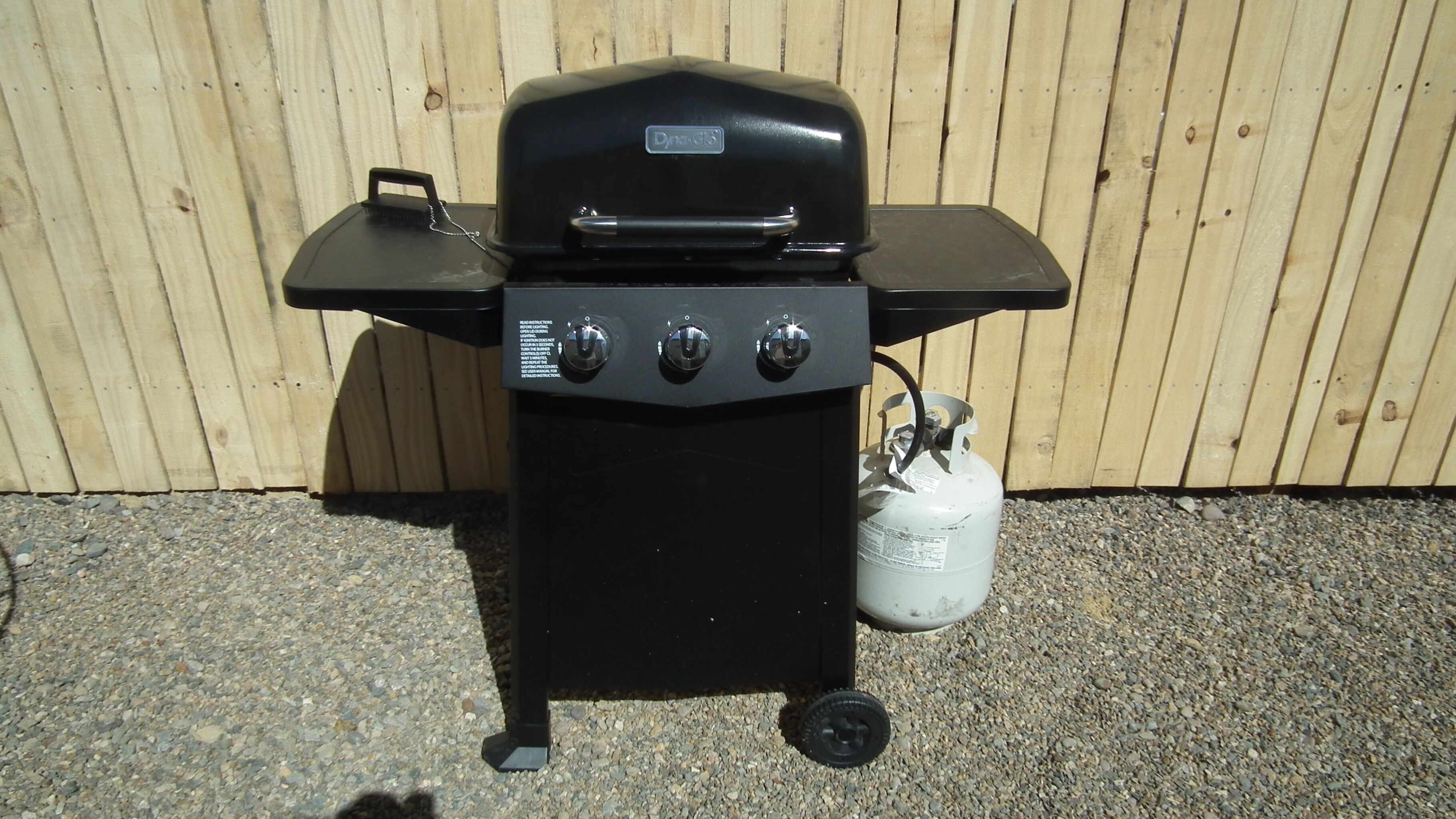 A black barbecue grill with three knobs and a propane tank.