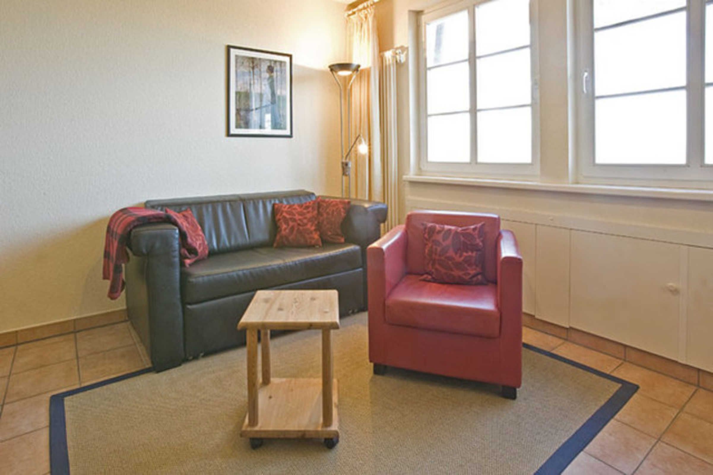 A living room with a sofa, a chair, a small table, a lamp, and a window.
