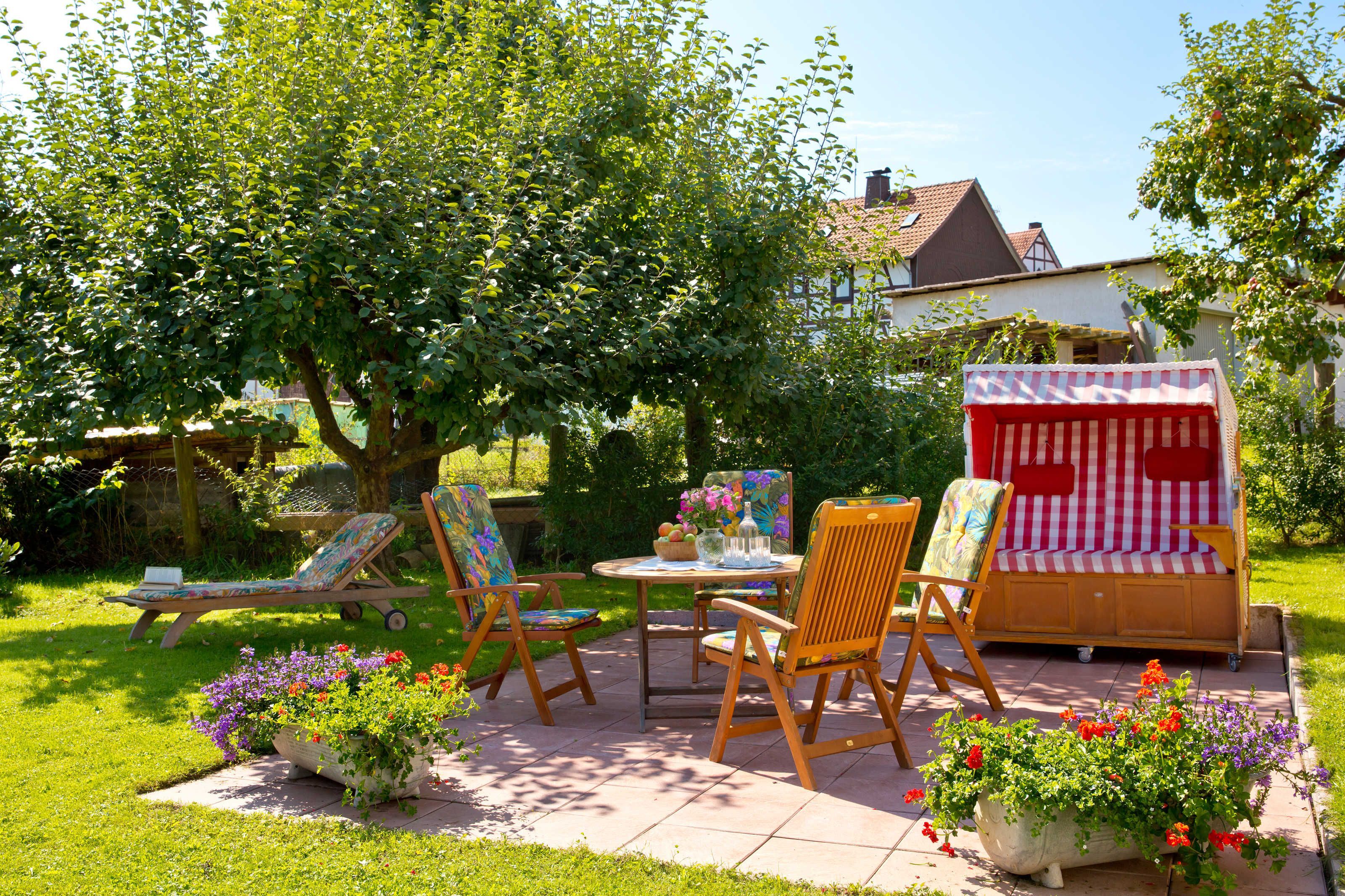 Un espace patio aménagé avec une table en bois, des chaises, un petit canapé et un auvent à rayures.
