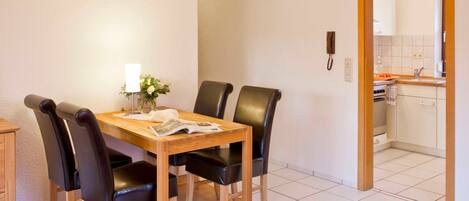 A dining area with a wooden table and four black chairs, a small vase with flowers, and a clock on the wall.