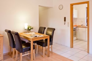 A dining area with a wooden table and four black chairs, a small vase with flowers, and a clock on the wall.