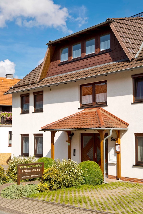 A two-story building with a brown tiled roof, a sign reading "Ferienwohnung," and a well-maintained garden in front.