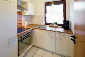 A compact kitchen with a stove, sink, and wooden countertop.