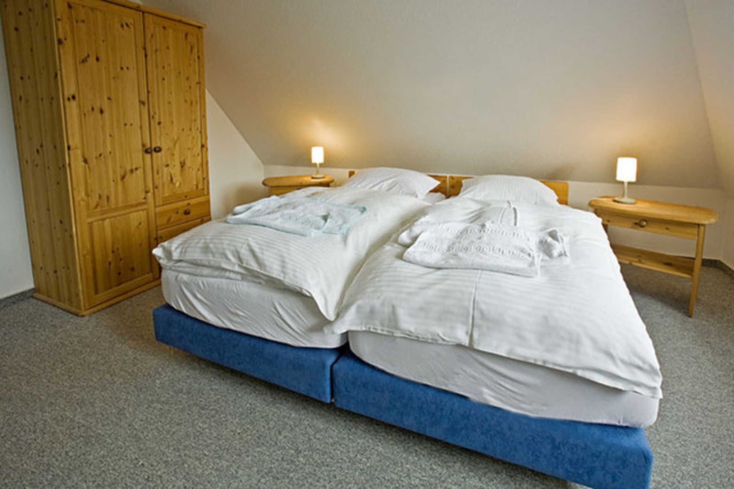 Un dormitorio con una cama grande, dos mesitas de noche con lámparas y un armario de madera.