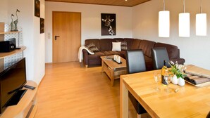 A modern living room with a wooden floor, a brown sofa, a wooden coffee table, and a dining table with a bottle of wine and glasses. - Apartment 3 - Apartment "am-edersee" (Edertal)