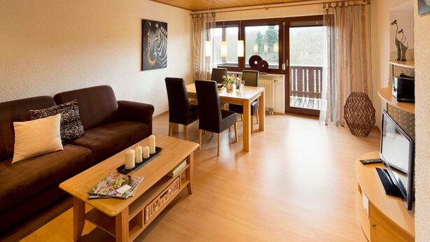 A modern living room with a brown leather sofa, wooden coffee table, and dining area with chairs and a table. - Apartment 3 - Apartment "am-edersee" (Edertal)