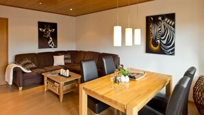 A modern living room with a brown sofa, a wooden dining table, and black chairs. There are two paintings on the wall, one of a giraffe and one of a zebra. - Apartment 3 - Apartment "am-edersee" (Edertal)