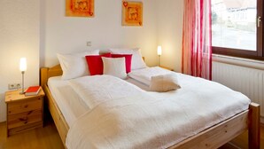 A neatly made bed with white and red bedding, a bedside table with a lamp, and two wall-mounted paintings. - Apartment 3 - Apartment "am-edersee" (Edertal)