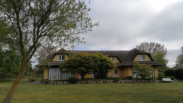 A two-story house with a thatched roof, surrounded by a well-maintained lawn and a stone wall.