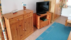 A wooden cabinet with drawers, a television on a wooden stand, and a blue rug on the floor.
