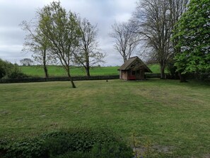A rural landscape with a small thatched-roof cottage, a grassy field, and trees.