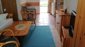 A cozy room with a wooden dining table, two wicker chairs, a blue rug, a wooden cabinet, and a television.