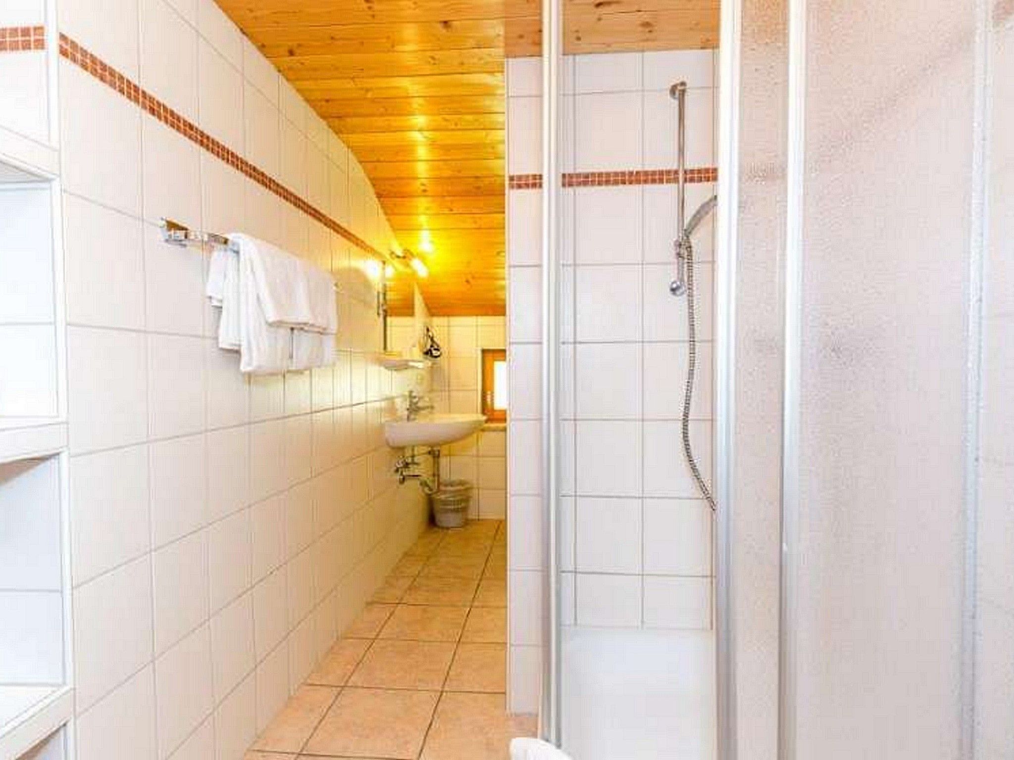Une salle de bain avec des murs recouverts de carreaux blancs, un plafond en bois, une douche et un lavabo.