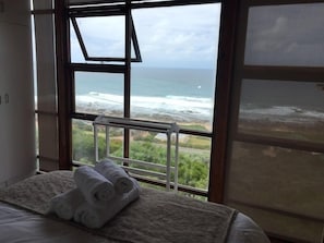Un dormitorio con un ventanal grande que da al océano, una cama con una toalla enrollada y un radiador blanco.