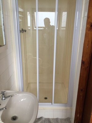 Un baño con cabina de ducha de vidrio, un lavabo blanco y un marco de puerta de madera.