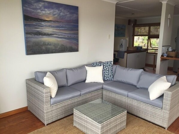 Una sala de estar moderna con un sofá seccional gris, una mesa de centro de vidrio y un cuadro abstracto grande en la pared.